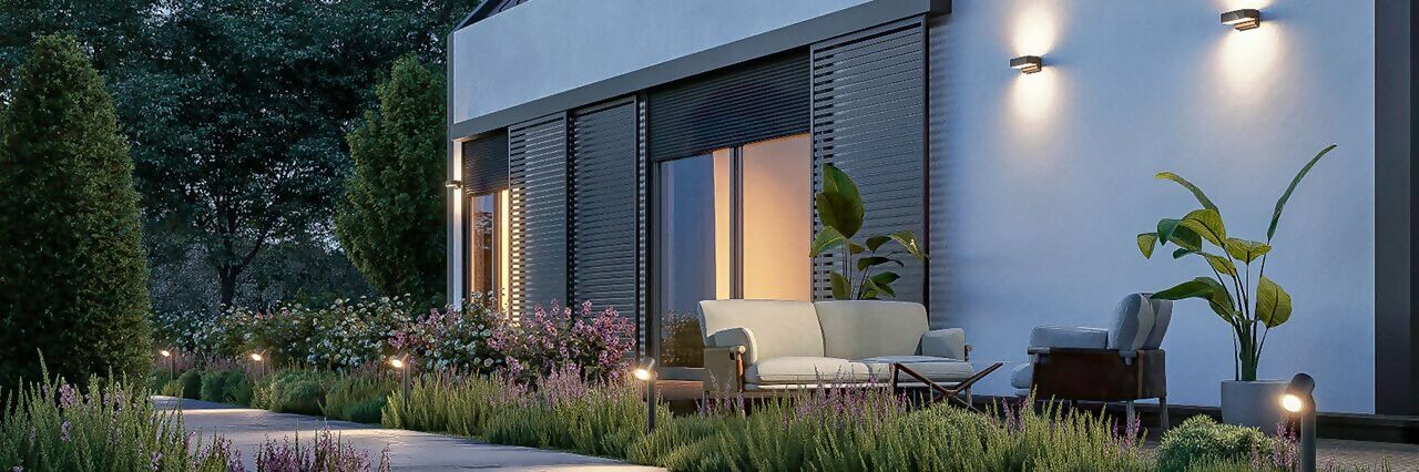 Jardin moderne illuminé avec des appliques murales et des luminaires de chemin pour une ambiance chaleureuse en soirée.