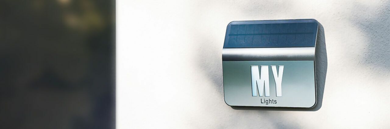 Plaque de numéro de maison solaire personnalisée montée sur un mur blanc, captant la lumière du jour pour une illumination autonome la nuit.