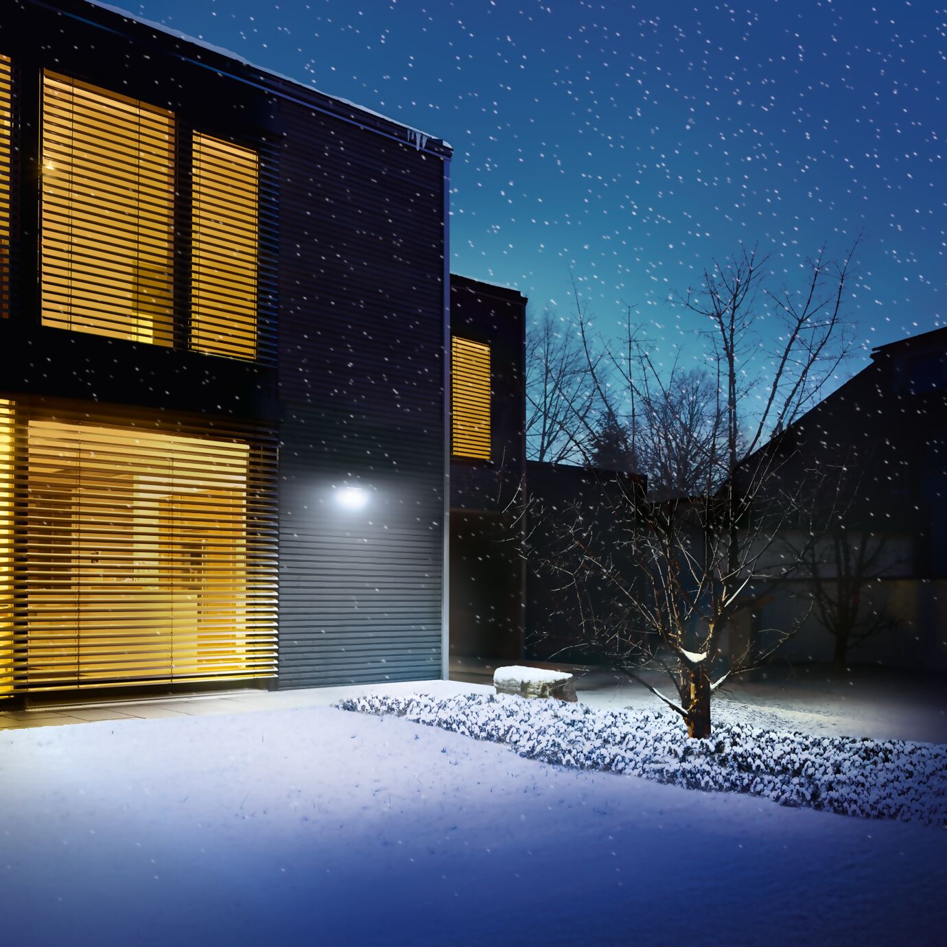 Maison moderne sous la neige avec un éclairage extérieur intelligent. Une applique murale LED activée par capteur éclaire la façade et le jardin, garantissant sécurité et visibilité par temps hivernal.