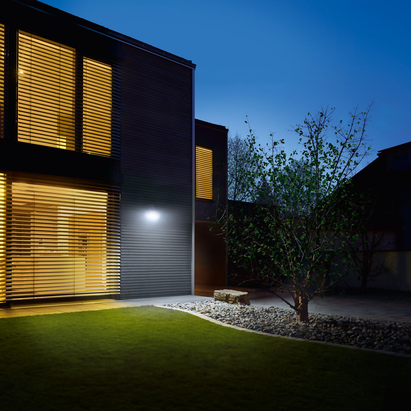 Maison moderne avec éclairage extérieur intelligent. Une applique murale LED s’active automatiquement à la tombée de la nuit, offrant sécurité et confort dans le jardin